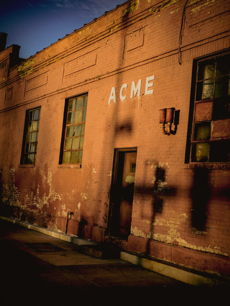 An abandoned building, the fading sunlight casting shadows on the brick walls.  ACME, a sign of things that once were.