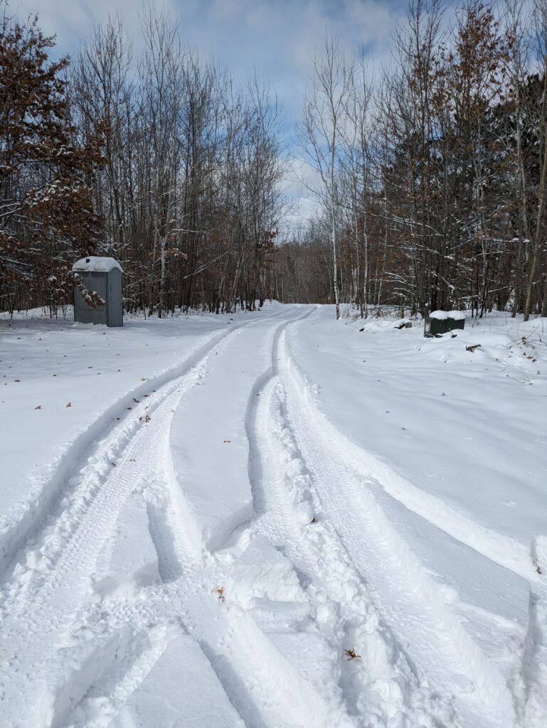 Deep tire tracks in fresh snow cutting through what looks like just trees.  There's also a port-a-potty.